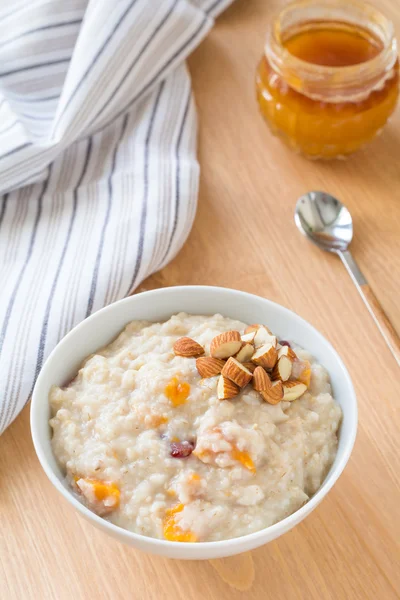 Oatmeal porridge with dried fruits, honey and nuts in bowl on breakfast table — Stock Photo, Image