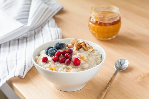 Oatmeal porridge with blueberries, cranberries and nuts in bowl on breakfast table — Stock Photo, Image