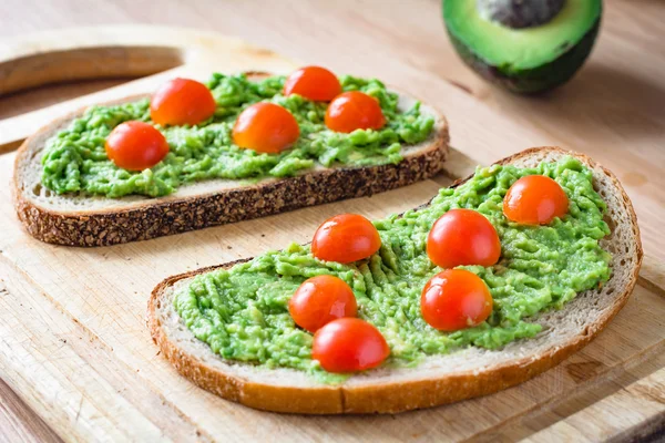 Ahşap kesme tahtası üzerinde püresi avokado ve kiraz domates ile tost