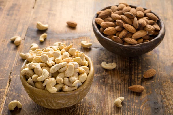 Healthy foods: bowl of cashews and almonds on wooden table — Stock Photo, Image
