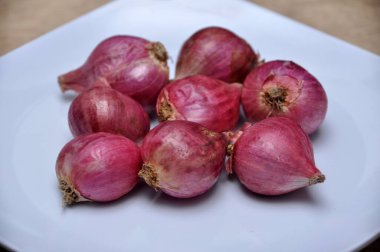 Mutfaktaki ahşap masada beyaz bir tabakta soğanlar.