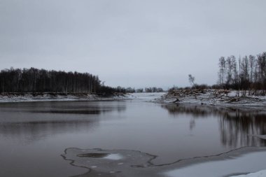 Donmuş nehir ve karlı kıyıları olan kuzey manzarası. Sert doğa - nehirdeki buz, soğuk su ve orman kıyıları.