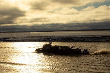 Sonbahar kuzey nehri gün batımında. Navigasyonun sonunda küçük bir gemi kuzey nehri boyunca yelken açar. Nehrin ortasındaki bir kumun üzerinde kar yatıyor..
