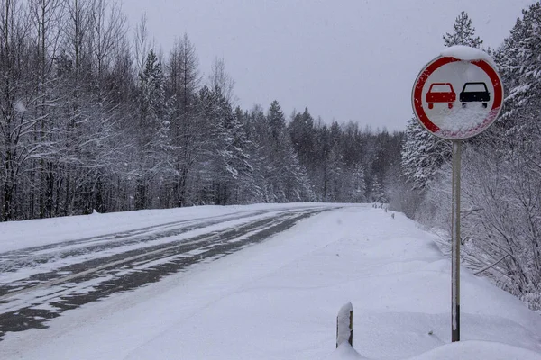 Overtaking on the opposite lane is prohibited. Road signs prohibiting overtaking in the opposite lane on the highway. The ice-covered winter track is dangerous. Drifts on the road.