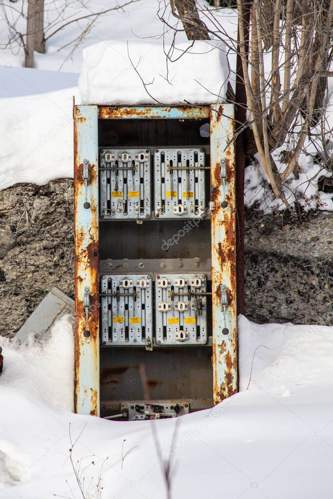 Rusty old distribution board among the snow. Abandoned large distribution board