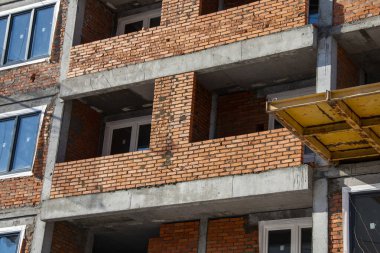 Çok katlı tuğla bina inşaatı. Bir vinç tarafından beton ve tuğladan yapılmış çok katlı bir bina inşa ediliyor..