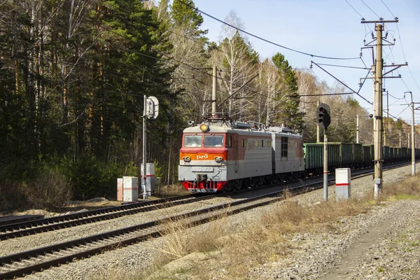 電気機関車が高い堤防に沿って突進する 貨物列車のある赤灰色の電気機関車 — ストック写真