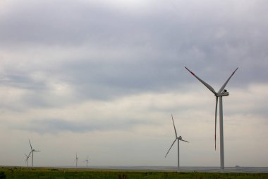 Endüstriyel rüzgar türbinleri ovada. Kocaman yel değirmenleri kasvetli bir gökyüzünün altında duruyor..