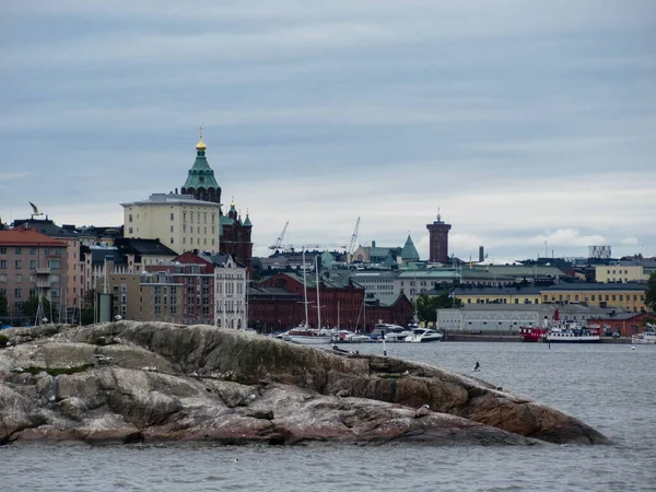 在多云的天气里 赫尔辛基市中心多彩的建筑物从大海中看去 岛上有一个小岛 有一只海鸥在空中飞翔 — 图库照片