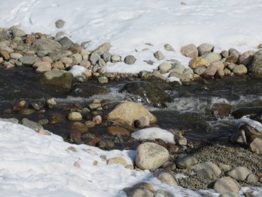 Karla çevrili bir parkta kayalık bir dere..