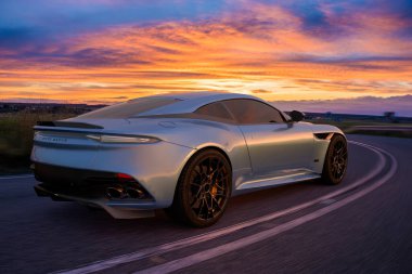 Aston Martin DBS süper leggera Gün batımında manzaralı bir yolda