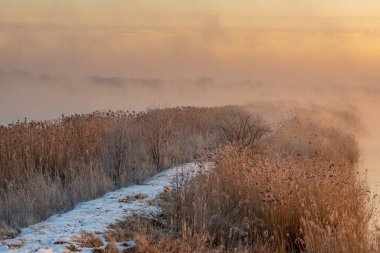 Soğuk ve sisli bir sabahta gölün üzerinde gün doğumu