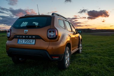 Dacia Duster, gün batımında çakıllı yolda küçük bir SUV kullanıyor.