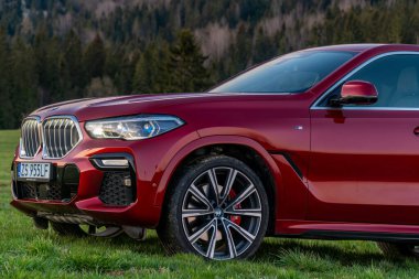 BMW X6 lüks SUV 'nin kaslı duruşu gün doğumunda bir dağ manzarasının arka planına karşı.