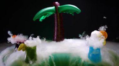 Plaj barında palmiye ağaçlı kuru buzlu çeşitli renkli kokteyller. Barmen gösterisi ve tropik bir adada buzlu kokteyl hazırladı. Kuru buz dumanı etkisi olan bir barda renkli içecekler.