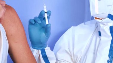 Bir hastanede Coronavirus aşısı aşısı. Covid-19 aşı konsepti. Hasta koruyucu giysi, maske ve güneşlik takan bir sağlıkçıdan kovan aşısı alıyor.. 