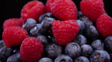 Siyah arka planda dönen ahududu ve yaban mersini yakından görülüyor. Taze, sert ve lezzetli böğürtlenler ve nane şekeri. Çiğ vejetaryen yaz atıştırmaları, orman meyveleri..