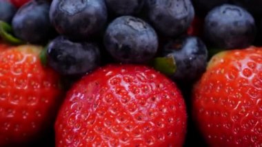 Siyah arka planda dönen çilek, ahududu ve yaban mersini. 4K 'da taze, organik orman meyveleri. Çiğ vejetaryen yaz atıştırması..