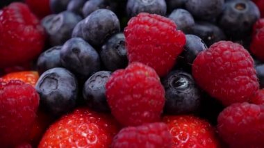 Siyah arka planda dönen çilek, ahududu ve yaban mersini. 4K 'da taze, organik orman meyveleri. Çiğ vejetaryen yaz atıştırması..