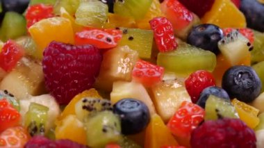 4K 'de siyah arka planda dönen renkli meyve salatası. Taze ve lezzetli meyveler, portakal, elma, böğürtlen, nar, kivi, ananas, ahududu, yaban mersini ve çilek