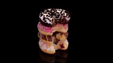 Isırılmış donutlar ve siyah arka planda dönen renkli serpinti. Çikolata soslu ve serpiştirilmiş tatlı donut. Kavram: tatlı yemek, fırın, abur cubur