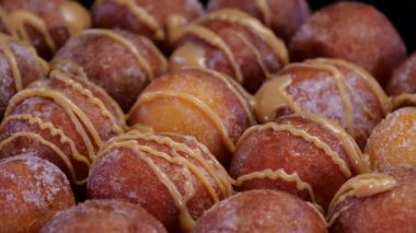 Köhne peynirli çörekler karamelli tatlı sosla kaplanmış, siyah arka planda dönüyor. Taze fırınlanmış kuark peynirinin üzerine karamel dökerek. Mini donut topları şekere bulanmış..