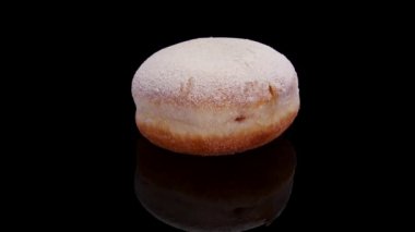 Pudra şekerli çörek ve siyah bir arkaplanda dönüyor. İzole edilmiş tatlı çörek. Kavram: tatlı yemek, fırın, abur cubur