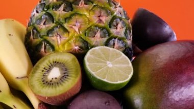 Turuncu bir zemin üzerinde tropikal ve egzotik meyveler, ananas tutkusu meyvesi, kivi, mango, limon, nar, portakal ve muz döner. Yaz meyveleri bileşimi.
