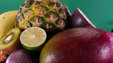 Yeşil zemin üzerinde tropikal ve egzotik meyveler, ananas tutkulu meyveler, kivi, mango, limon, nar, portakal ve muzlar dönüyor. Yaz meyveleri bileşimi.