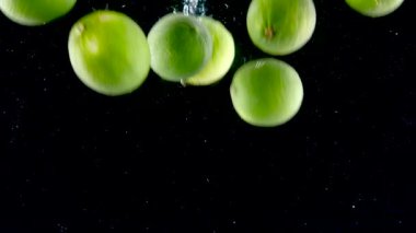 Limon yavaş çekimde suya sıçrıyor. Siyah arka planda yavaş yavaş düşen bir sürü limon. Siyah arka planda izole edilmiş organik yeşil turunçgil. Meyveli taze su.