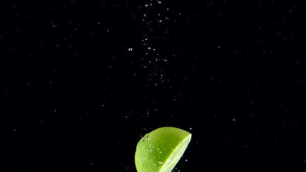 石灰缓慢地飞溅入水中 完美的绿色石灰缓缓落在黑色的背景上 在黑色背景上分离的有机绿色柑橘 有水果的淡水 — 图库视频影像