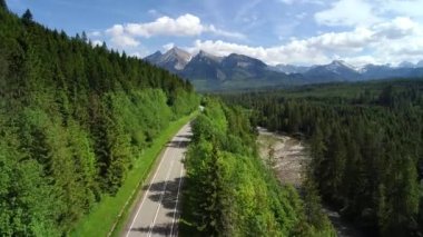 Çevredeki dağlık yolun ve kayalık nehrin havadan görünüşü. Dağ sırasına ve kayalık dereye giden yolun sinematik drone görüntüsü. Alp görünümü.