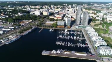 Modern bir sahil şehrinde beyaz yatlar ve yelkenlilerle dolu liman manzarası. Yazın güneşli bir günde tekneli Marina. Arka planında gökdelenler olan modern bir kasabada iskele..