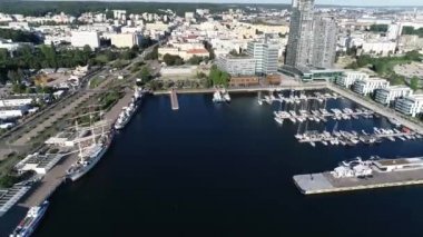 Modern bir sahil şehrinde beyaz yatlar ve yelkenlilerle dolu liman manzarası. Yazın güneşli bir günde tekneli Marina. Arka planında gökdelenler olan modern bir kasabada iskele..