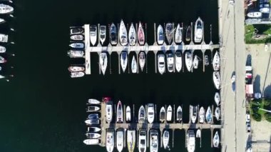 Modern bir sahil şehrinde beyaz yatlar ve yelkenlilerle dolu bir liman manzarası. Yazın güneşli bir günde tekneli Marina. Arka planında gökdelenler olan modern bir kasabada iskele..