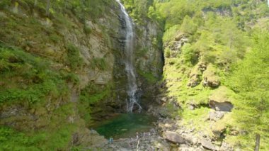 Sonogno kasabasının yakınlarındaki şelalenin etrafında toplanan insanlar. Dondurucu soğuk şelale. Froda Şelalesi, Verzasca Vadisi, Canton Ticino, İsviçre