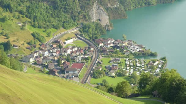 湖や山に囲まれた小さなスイスの町を介して車や列車のトラフィックの空中ビュー Lakeルツェルン シシコン カントン スイス — ストック動画