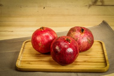 Üç olgun nar meyvesi. Kırmızı büyük narlar. Ahşap tepside, altında masa örtüsü olan nar. Tam nar meyvesi..