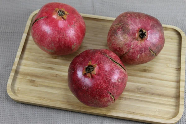Three ripe pomegranate fruits. Red large pomegranates. Pomegranates on a wooden tray, with all the tablecloth underneath. Whole pomegranate fruit.
