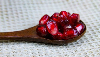 Tahta bir kaşıkta nar tohumlarını yakın çekim. Ahşap kaşık, keten peçetenin üzerinde kırmızı olgun nar tohumları. Tahta kaşıkta nar tohumları..