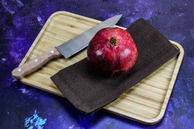 Mavi arka planda, ahşap bir tepside peçete / kumaş üzerinde tam nar meyvesi. Büyük, kırmızı, olgun, bıçaklı, açılmaya hazır bir nar. Sağlıklı yaşam kavramı. Meyveli nar..