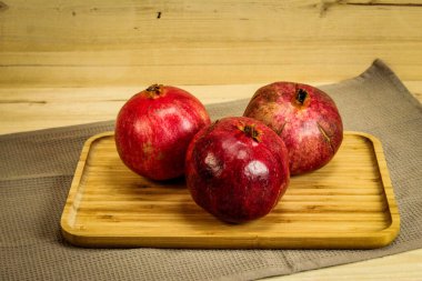 Üç olgun nar meyvesi. Kırmızı büyük narlar. Ahşap tepside, altında masa örtüsü olan nar. Tam nar meyvesi..