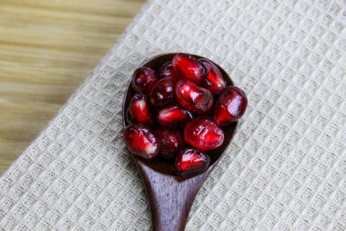 Tahta bir kaşıkta nar tohumlarını yakın çekim. Ahşap kaşık, keten peçetenin üzerinde kırmızı olgun nar tohumları. Tahta kaşıkta nar tohumları..
