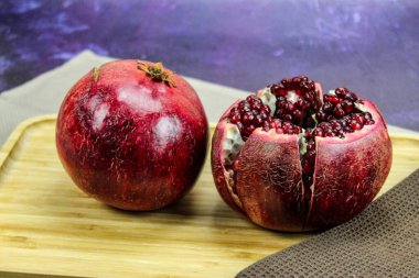 İki büyük kırmızı nar meyvesi. Tam kırmızı, olgun bir nar. Nar meyvesi beş parçaya ayrılır ve mavi arka plandaki ahşap tepside bir arada tutulur..