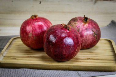 Üç olgun nar meyvesi. Kırmızı büyük narlar. Ahşap tepside, altında masa örtüsü olan nar. Tam nar meyvesi..