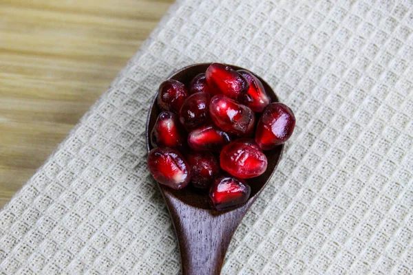 Tahta bir kaşıkta nar tohumlarını yakın çekim. Ahşap kaşık, keten peçetenin üzerinde kırmızı olgun nar tohumları. Tahta kaşıkta nar tohumları..