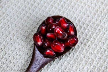 Tahta bir kaşıkta nar tohumlarını yakın çekim. Ahşap kaşık, keten peçetenin üzerinde kırmızı olgun nar tohumları. Tahta kaşıkta nar tohumları..