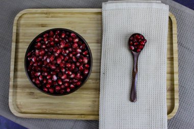 Tahta bir kâse içinde kırmızı nar tohumları ve yanında peçetenin yanındaki tohumlarla birlikte tahta bir kaşık. Tahta tepside servis edilen kırmızı nar tohumları..