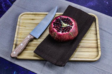 Mavi bir zemin üzerinde ahşap bir tepside peçete / kumaş üzerinde tüm nar tabağının tepsisini kes. Yanında bıçak olan büyük, kırmızı, olgun bir nar. Sağlıklı yaşam kavramı. Meyve..