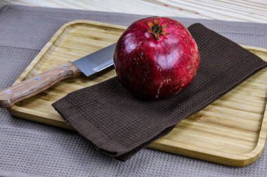 Masadaki ahşap tepside peçete / kumaş üzerinde tam nar meyvesi. Yanında bıçak olan büyük kırmızı bir nar, açılmaya hazırdı. Sağlıklı yaşam kavramı. Meyveli nar..